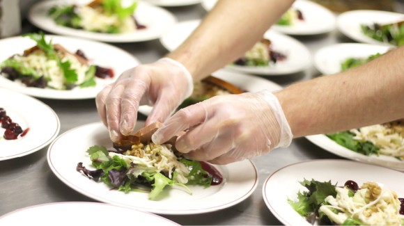 Restaurantküche, in der viele weiße Teller zusehen sind, auf denen Salat draufgelegt wird